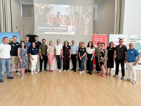 Organisatorinnen, Organisatoren und Unterstützende der Veranstaltung stehen gemeinsam für ein Gruppenfoto vor der Präsentationsleinwand.