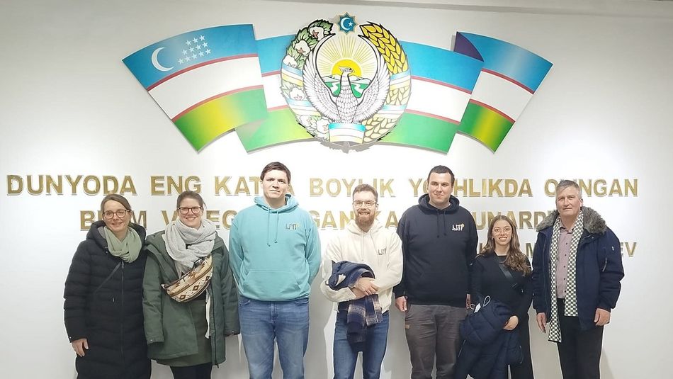 Professor, Mitarbeitende und Studierende der Fachrichtung Lebensmitteltechnik an der Agrar-Univerität in Taskent, Gruppenbild mit sieben Personen vor einer Wand mit einer usbekischen Flagge 