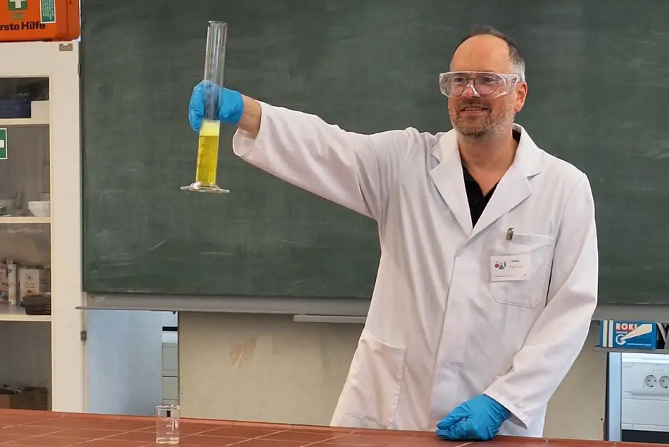 KinderUni an der Hochschule Trier in der Lebensmitteltechik - Prof. Dr. Heiko Oertling zeigt vorne am Laborpult einen Versuch in dem er ein Messkolben hochhält, dieser ist teilweise mit einer gelben schäumenden Flüssigkeit gefüllt