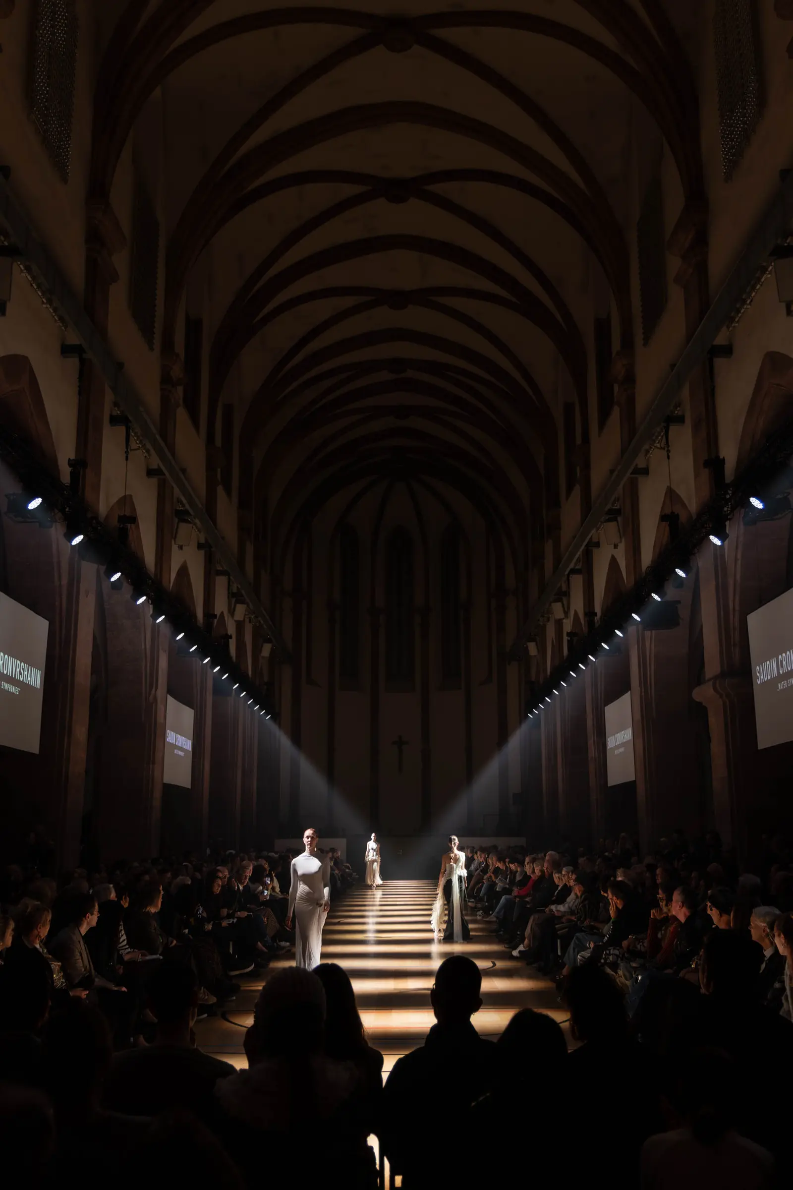 Models präsentieren Mode auf einem beleuchteten Laufsteg in der historischen Kirche St. Maximin.