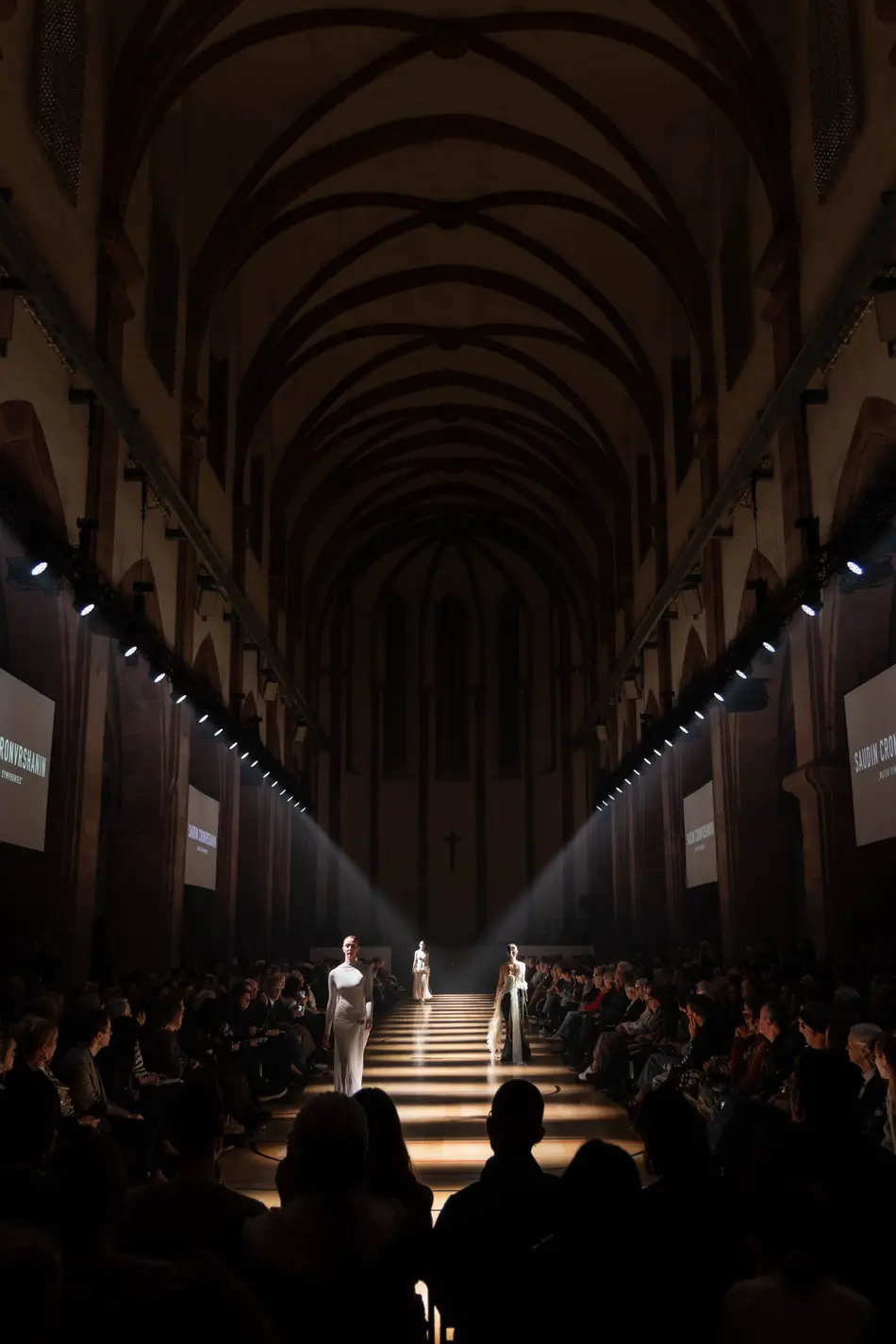 Models präsentieren Mode auf einem beleuchteten Laufsteg in der historischen Kirche St. Maximin.