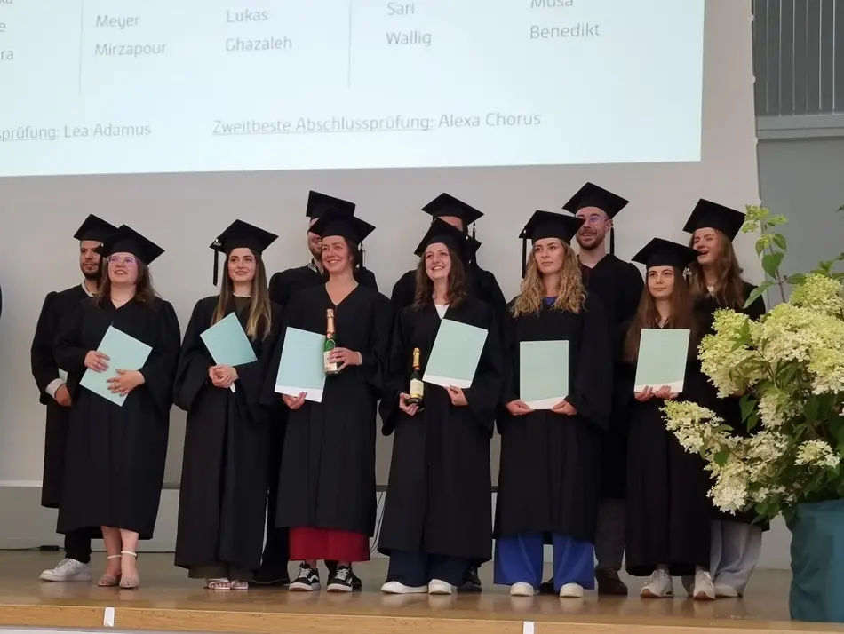 Bachelor-Absolvierende stehen in einer Gruppe mit Talaren 