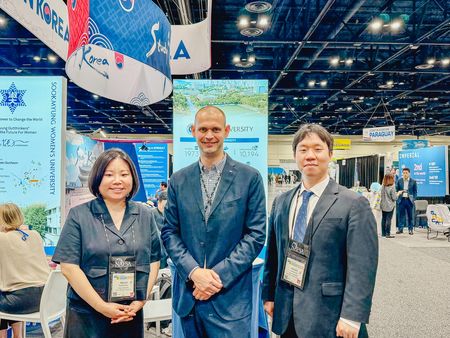 Drei Personen in Businesskleidung stehen auf einer internationalen Bildungsmesse vor einem Korea-Stand und blicken in die Kamera.