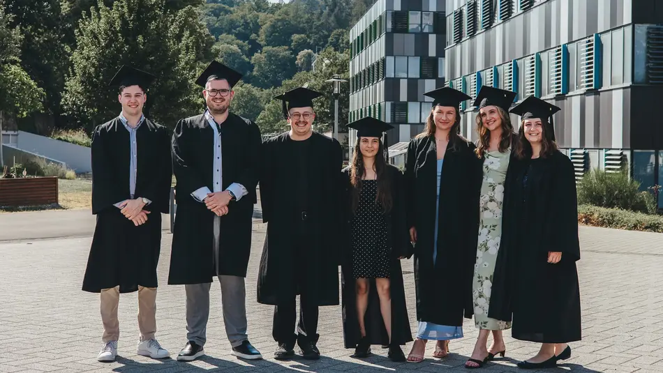 Absolvierende des Master Lebensmittelwirtschaft stehen auf dem Campus der Hochschule Trier in Talaren