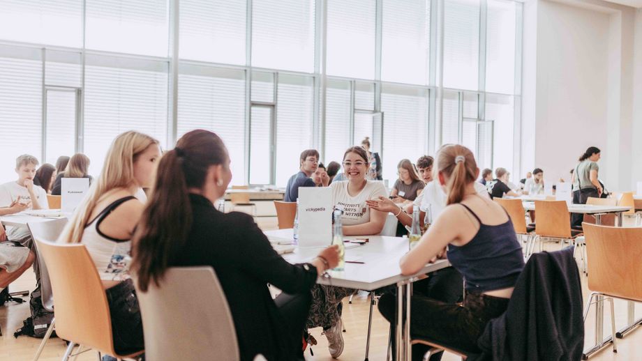 Studierende sitzen in Gruppen an Tischen in einem hellen Seminarraum und arbeiten gemeinsam an einer Aufgabe.
