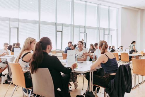 Studierende sitzen in Gruppen an Tischen in einem hellen Seminarraum und arbeiten gemeinsam an einer Aufgabe.