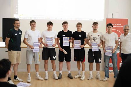 Junge Teilnehmer stehen mit Urkunden in einer Reihe vor der Leinwand und posieren für ein Gruppenfoto.