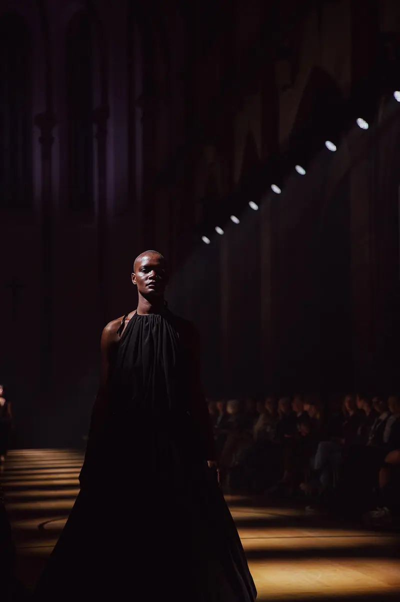 Model in einem bodenlangen schwarzen Kleid im Scheinwerferlicht.