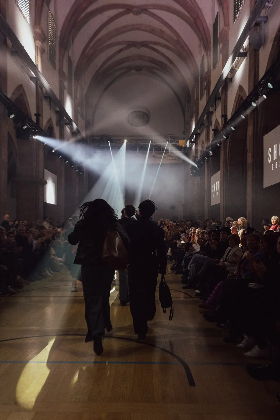 Models präsentieren Mode auf einem beleuchteten Laufsteg in der historischen Kirche St. Maximin
