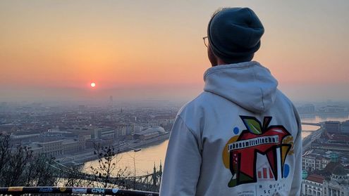 ein Studierender steht mit dem Rückn zur Kamera und blickt während des Sonnenuntergangs auf die Stadt Budapest